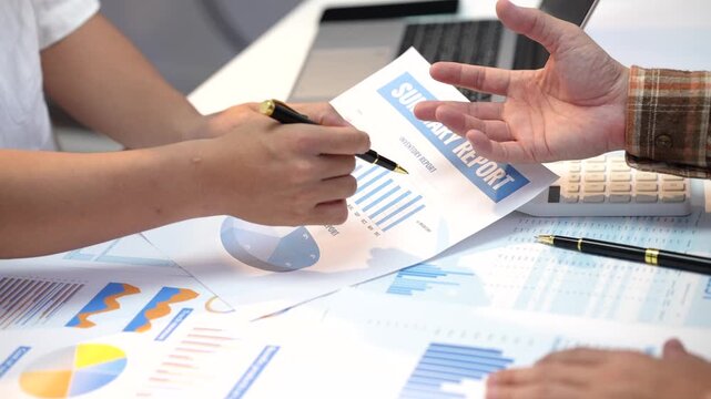 Business team reviewing a summary report with charts, graphs, calculator and laptop on a desk during a financial planning meeting.