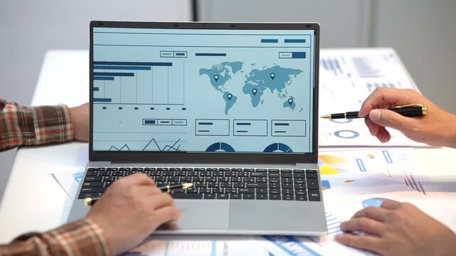 Business team reviewing global analytic on a laptop, with charts, reports and notes spread across a desk during a planning meeting.