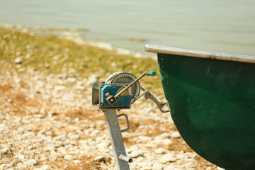  Boat winch mechanism next to a green rowboat on a stony shore © Tsend-Ayush
