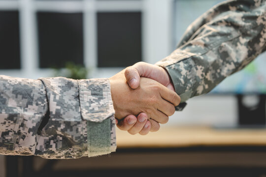Close-up of two military service members in digital camouflage uniforms shaking hands indoors, showing teamwork, respect, agreement and partnership.