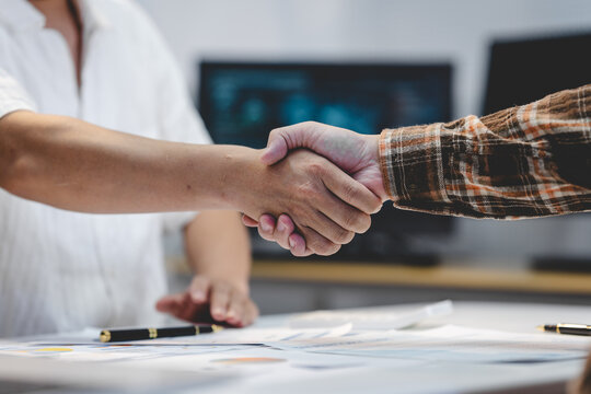 Close-up of two businesspeople shaking hands over documents on an office desk, showing agreement, partnership, and successful teamwork.