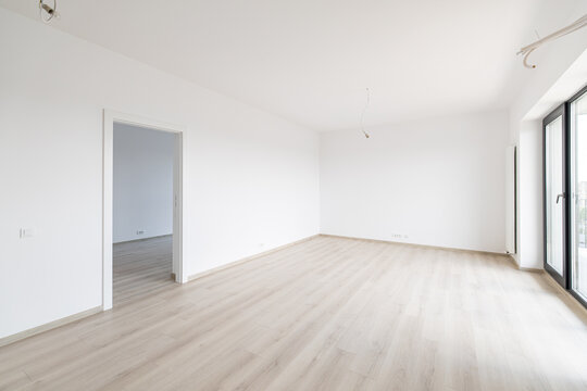 Bright empty modern apartment interior with clean white walls, light laminate wood floor, large window bringing natural daylight, ready for new home moving.