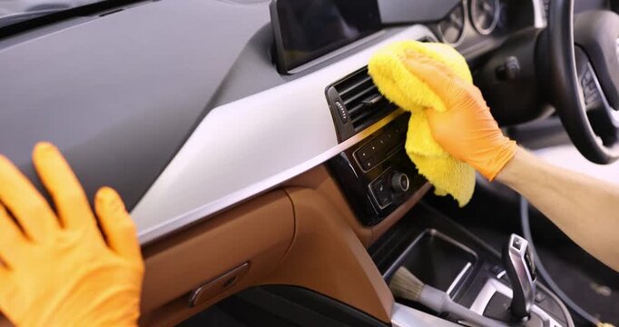 Hands diligently polish the interior of a car in a well-lit garage. With soft cloths and orange gloves, every detail shines bright, showcasing skill and attention.