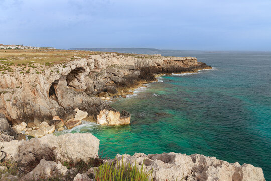 Rugged coastal cliffs meet turquoise sea waters under a vast sky
