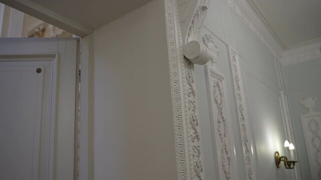 White paneled door opening beside ornate classical plaster wall with Greek key border and acanthus corbel, with door, ajar, doorframe, panel detail, showing molding, trim, plaster, ornament context