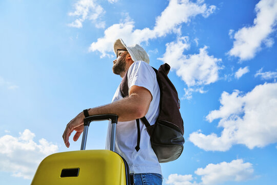 Low Angle View of Male Traveler with Backpack and Yellow Suitcase Against Blue Sky