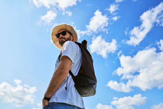 Low angle view of male traveler with backpack and hat against blue sky