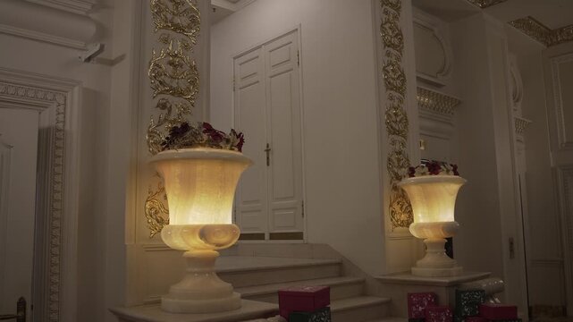 Ornate foyer with illuminated alabaster urn lamps flanking marble staircase under gilded pilasters, with interior, foyer, alabaster, lamp detail, showing urn, marble, staircase, door context