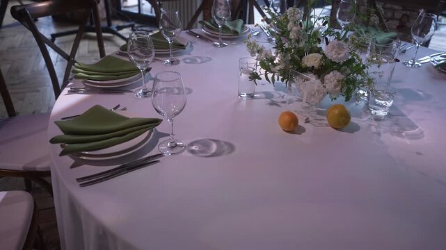 Elegant banquet table with floral centerpiece and subtle object adjustments under soft colored light, with table, banquet, place, setting detail, showing napkin, plate, glass, wineglass context