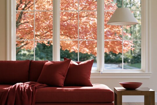 Cozy autumn living room seating with deep red sofa and window bowl beside sunlit maple foliage for seasonal wallpaper and background design