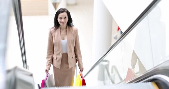 A confident woman descends the escalator in a busy mall, gracefully carrying colorful shopping bags. Her smile reflects excitement and delight in the bustling atmosphere.