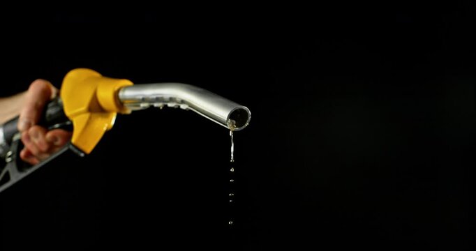 Super slow motion (1000 fps) fuel drops dripping from gasoline nozzle, symbol of depletion and fuel shortage. Minimal liquid flow on black background, dramatic lighting, energy crisis concept.