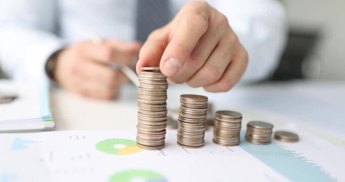 A person in a crisp shirt focuses intently while stacking coins in a neat arrangement on a desk. The cheerful office buzzes with energy as colorful graphs spread out.
