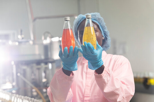 Black woman inspecting drink quality with rows of glass bottles on the automated conveyor system in manufacturing assembly line.
