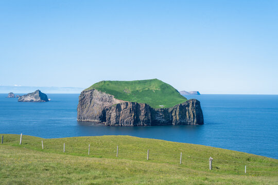 A scenic view of the famous lonely white house on the green grassy cliffs of Ellidaey Island surrounded by the blue ocean in Vestmannaeyjar, Iceland.
