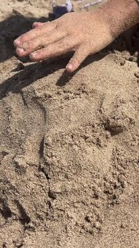 Child hand touches and shapes wet sand on a sandy beach. Summer vacation, child playing, beach fun.