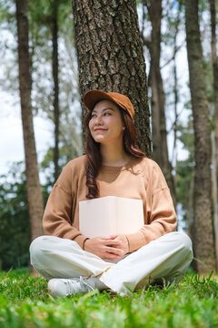 Vertical portrait image of a woman holding and reading a book while sitting in the park