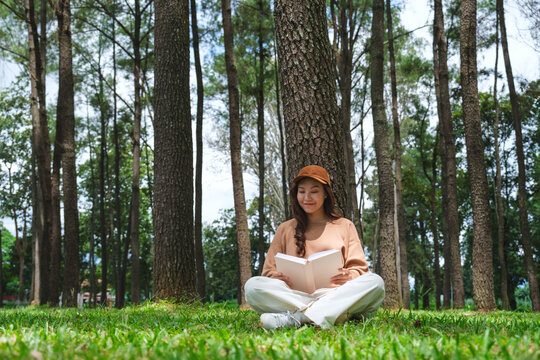 Portrait image of a woman reading a book while sitting in the park