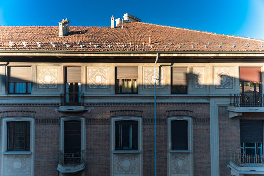 Facciata in mattoni di edificio storico con finestre simmetriche, balconcini e motivi geometrici. La luce naturale evidenzia texture e dettagli architettonici. Ideale per temi urbani e architettura