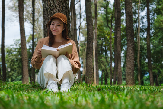 Portrait image of a woman reading a book while sitting in the park