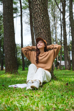 Vertical portrait image of a woman sitting and putting hands behind her neck for relaxing in the park
