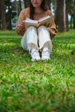 Vertical closeup image of a woman reading a book while sitting in the park