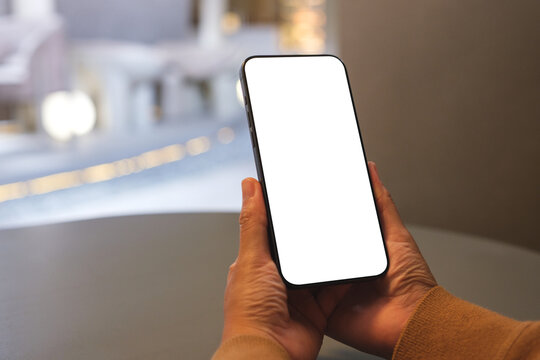 Mockup image of a woman holding mobile phone with blank desktop screen in cafe