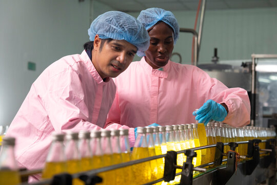 Two factory workers monitoring cold drink bottles on production line at drinks production plant.