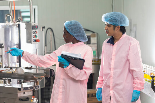 Two factory workers monitoring cold drink bottles on production line at drinks production plant.