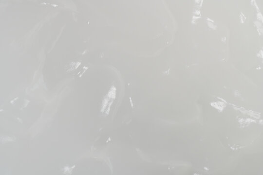 Macro top view of white cosmetic cream texture with soft wavy pattern and glossy light reflections, full frame smooth moisturizer background for luxury skincare concepts.