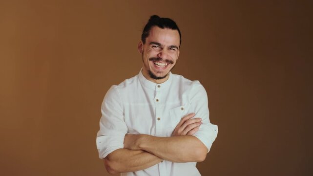 Head-and-torso motion showing young man standing with arms crossed while facial expression shifts from gentle smile to broad grin with slight head tilt and subtle forward lean, body language remains