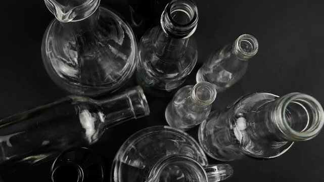 Small transparent glass bottles of various shapes stand on a black background, versatile containers used for storage of different objects and liquid. Glass bottles collection, top view
