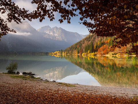 Autumn leaves frame Predil Lake reflecting Julian Alps, a nature tourism destination for travel and outdoor exploration, offering copy space. Julian Alps,Predil lake,Tarvisio,Friuli,Italy.