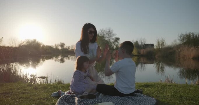 Family rest near Lake. Young mother spend time with children son and daughter enjoying nature. 4K 10-bit