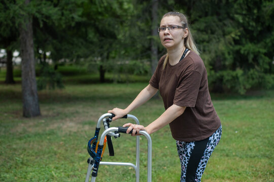 A young woman with cerebral palsy walks in a park with a walker.