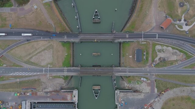 Top down aerial drone view of the Afsluitdijk crossing the Lorentz Locks in the Netherlands, showing cars and trucks driving over the road above the water and lock infrastructure.