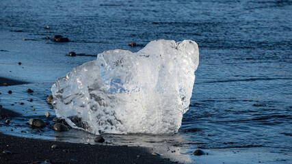 Melting ice from Vatnajokull Glacier drifts onto the black sand shore of Diamond Beach, Iceland, showing ancient glacial ice and the effects of ongoing climate change. © Asanee