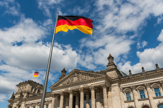 Deutschlandfahnen wehen im Wind vor dem Deutschen Reichstag bei Sonnenschein und blauem Himmel, Berlin
