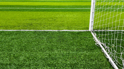 Green artificial turf with a white goal post and net outlining a soccer field, close up low angle view emphasizing texture, lines, sport, training and outdoor play © Newleks