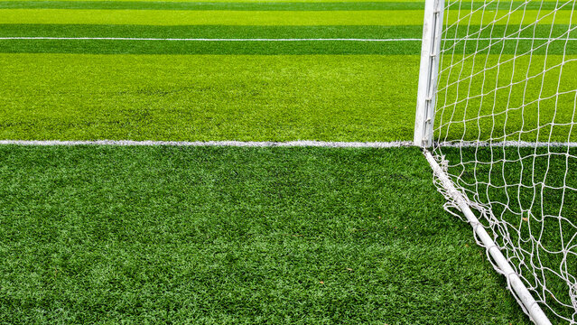Green artificial turf with a white goal post and net outlining a soccer field, close up low angle view emphasizing texture, lines, sport, training and outdoor play