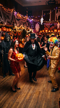 People in Halloween costumes dancing and celebrating, with pumpkins and spooky decorations, representing a festive party atmosphere