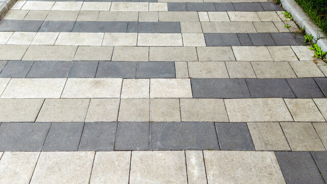 Pavement with interlocking concrete pavers creating a striped pattern in light gray and dark gray tones, forming an urban pathway or walkway texture and background