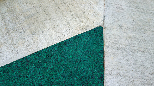 Concrete pavement sections connecting with a dark green artificial grass area, forming clean lines and a modern, abstract geometric pattern on the ground surface