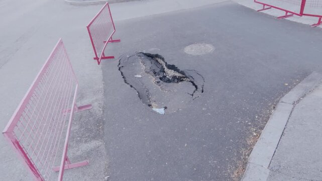 neutral roadside pothole with red triangular warning sign observed on concrete pavement under static ground-level perspective, safety infrastructure maintenance context.