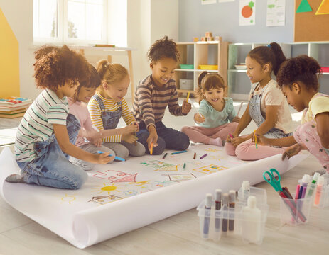 A diverse group of young children happily drawing and coloring together on a large paper roll in a bright classroom setting, fostering creativity and collaboration.