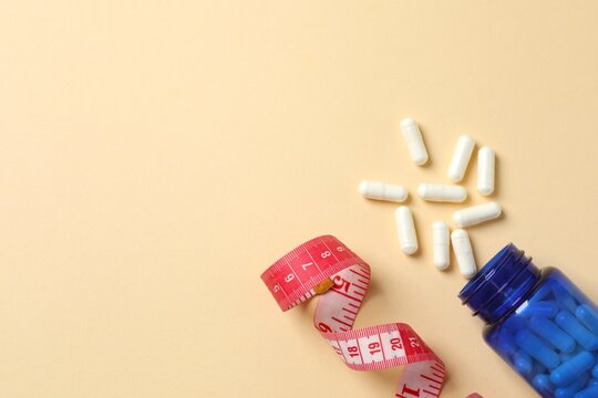 Jar of weight loss pills and measuring tape on color background, flat lay. Space for text