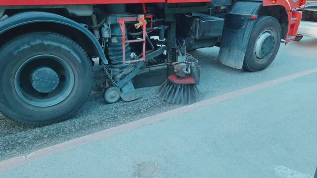Close up shot of a mechanical rotating disc brush with water spraying on a municipal sweeper truck washing and cleaning a city street