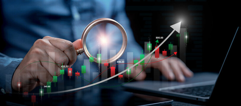 Investor hand holding magnifying glass analyzing stock market data chart with rising growth arrow on laptop for investment strategy and financial research concept. digital financial diagram. BI.