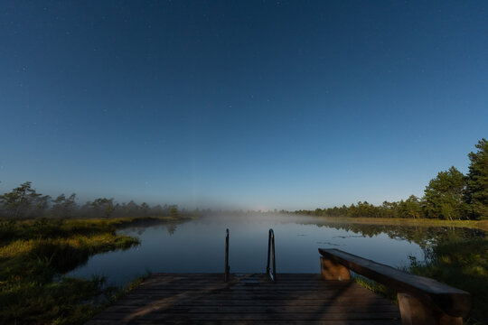 Wooden swimming dock with a metal ladder on Lao jarv lake in Omma raba bog under a starry night sky and moonlight in Estonia.