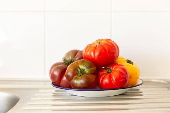 Des tomates rouges et jaunes empil&eacute;es sur une assiette blanche pos&eacute;e sur un &eacute;vier de cuisine en inox